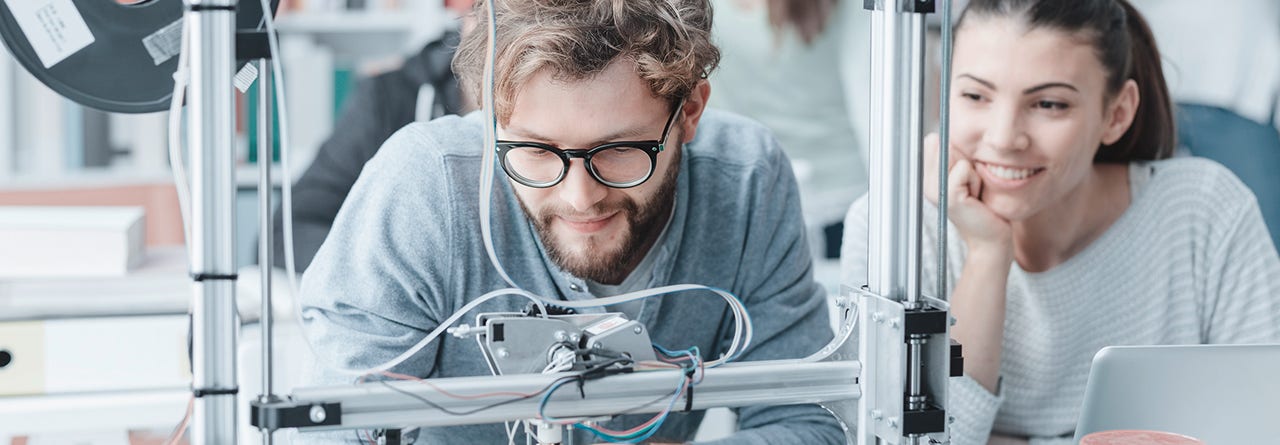 A smiling engineer woman and man working in a laboratory on a 3D printer project.