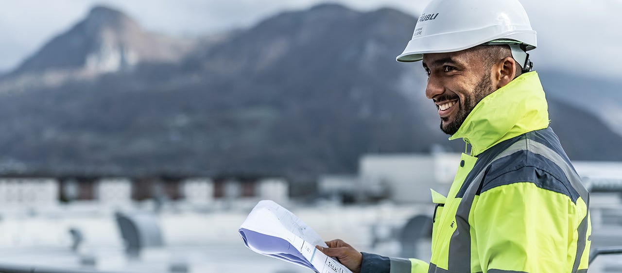 Man inspecting the roofs of Stäubli production unit, a document in the hands and mountains in the background.