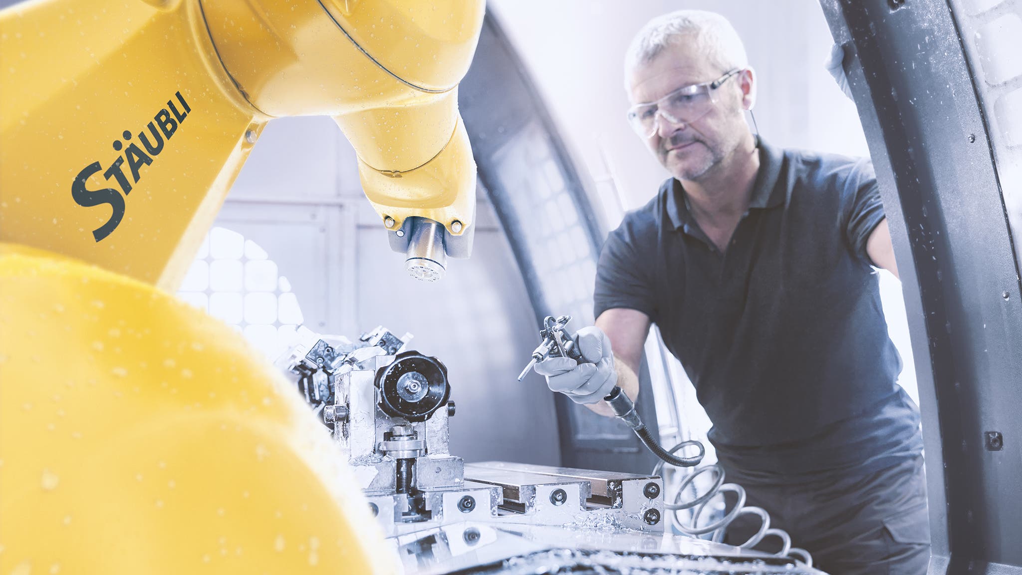 Industrial robot inside a computer numerical controlled (CNC) for machine tending application. An operator cleans the chips.